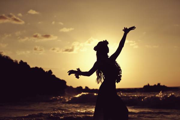 A woman hula dances on the beach during sunset