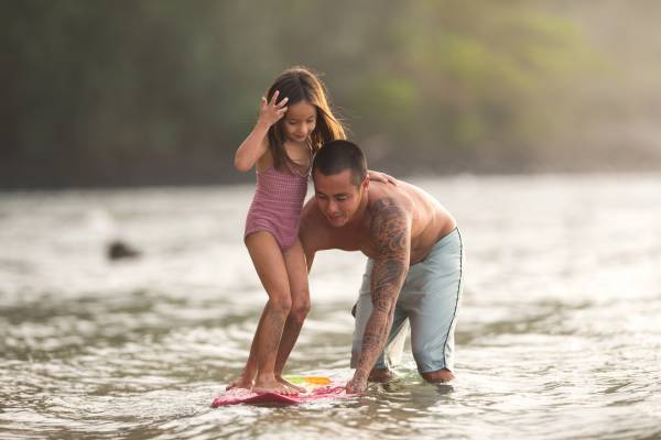 A father teaches his young daughter how to surf on calm waters